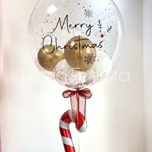 Balão transparente de 50 cm, personalizado com mensagem natalina, glitter, confetes e balões internos, com detalhe de balão em formato de doce bengala e laço natalino decorativo.
