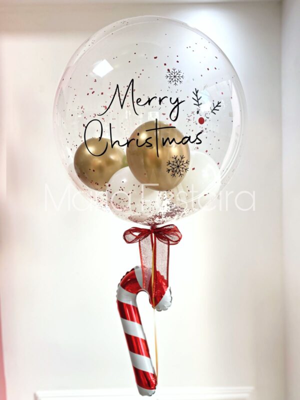 Balão transparente de 50 cm, personalizado com mensagem natalina, glitter, confetes e balões internos, com detalhe de balão em formato de doce bengala e laço natalino decorativo.
