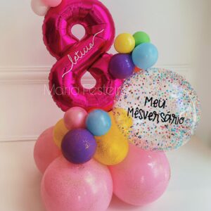 Arranjo de mesversário com balão número metalizado personalizado, balão bolha com confetes coloridos e base decorativa com balões vibrantes.