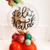 Balão transparente personalizado com glitter e confetes, base de balões descontruídos e fita decorativa natalina, ideal para decoração de Natal.