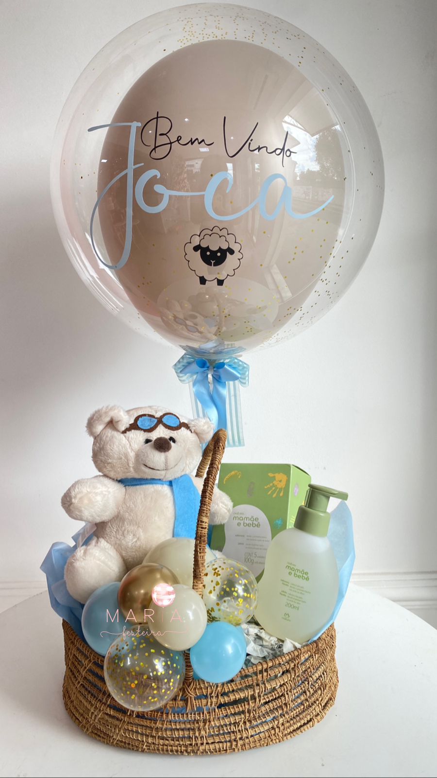 Cesta de presente maternidade contendo balão Bubble personalizado com confetes, urso de pelúcia, Kit Mamãe e Bebê Natura e base decorativa com mini balões em tons pastéis.