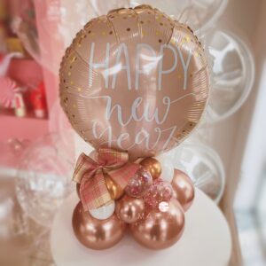 Arranjo de mesa Feliz Ano Novo com balão personalizado em folha de ouro rosa, base de balões desconstruídos e laço decorativo especial