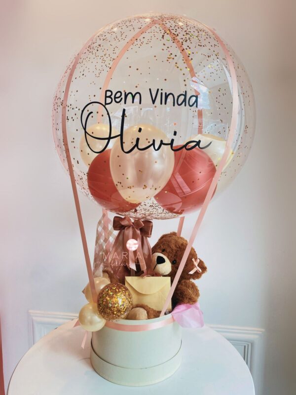Box de maternidade com balão transparente decorado com confetes, ursinho de pelúcia e caixa neutra decorativa, com a frase "Bem-vinda, Olivia"