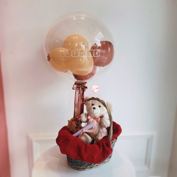 Arranjo de maternidade com ursinho de pelúcia, cesta decorada e balão personalizado com o nome do bebê, adaptável para meninos e meninas.