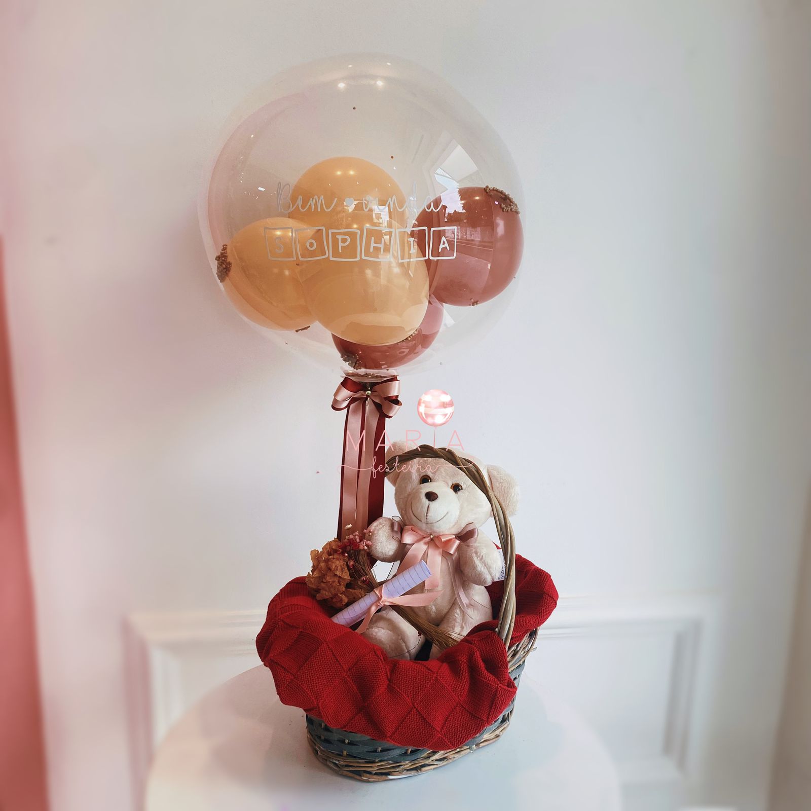 Arranjo de maternidade com ursinho de pelúcia, cesta decorada e balão personalizado com o nome do bebê, adaptável para meninos e meninas.