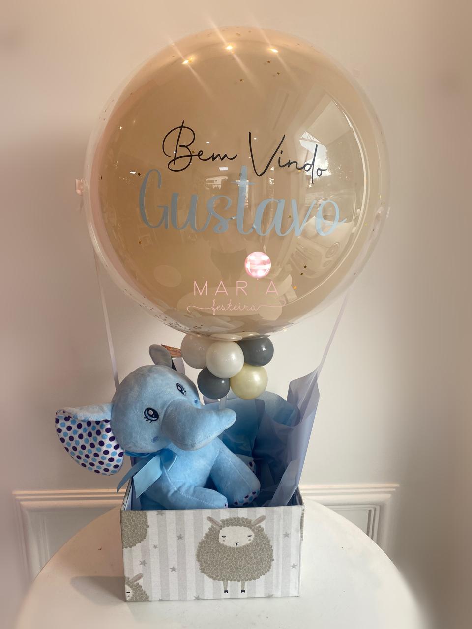 Kit de boas-vindas com elefantinho de pelúcia azul, balão transparente personalizado com nome, e caixa decorativa com estampa de ovelhas.