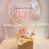 Imagem de presente “Bem-Vindo com Carinho”, com ursinho de pelúcia e balão bubble transparente decorado com confetes, ideal para ocasiões de boas-vindas.