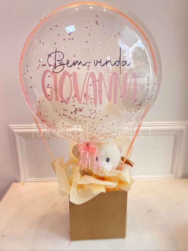 Imagem de presente “Bem-Vindo com Carinho”, com ursinho de pelúcia e balão bubble transparente decorado com confetes, ideal para ocasiões de boas-vindas.