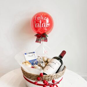 Cesta de Natal com vinho tinto, chocolates Lindt, Ferrero Rocher, Mini Bubble personalizada e bolinha acrílica decorativa, ideal para presentear com sofisticação.