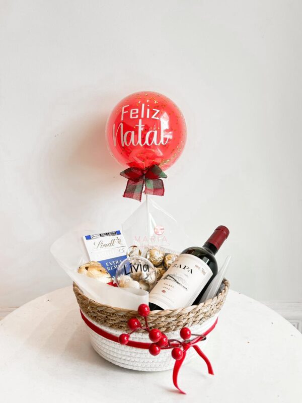 Cesta de Natal com vinho tinto, chocolates Lindt, Ferrero Rocher, Mini Bubble personalizada e bolinha acrílica decorativa, ideal para presentear com sofisticação.