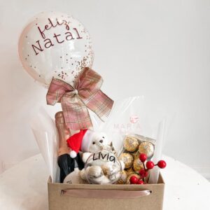 Cesta natalina personalizada com ursinho de pelúcia, balão decorado com confetes dourados e mensagem de Feliz Natal, espumante e bombons Ferrero Rocher.