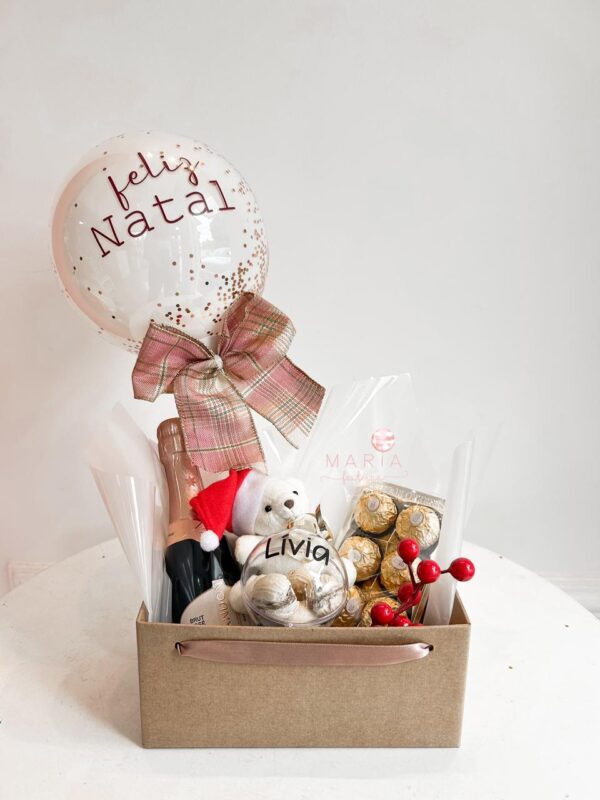 Cesta natalina personalizada com ursinho de pelúcia, balão decorado com confetes dourados e mensagem de Feliz Natal, espumante e bombons Ferrero Rocher.