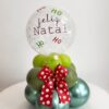 Arranjo de mesa natalino com base em formato de mini árvore de balões, laço decorativo vermelho com poás brancos e mini bubble transparente personalizado com ‘Feliz Natal’ e ‘Ho Ho Ho’.