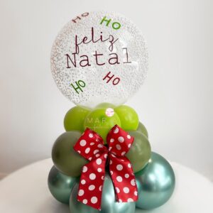 Arranjo de mesa natalino com base em formato de mini árvore de balões, laço decorativo vermelho com poás brancos e mini bubble transparente personalizado com ‘Feliz Natal’ e ‘Ho Ho Ho’.