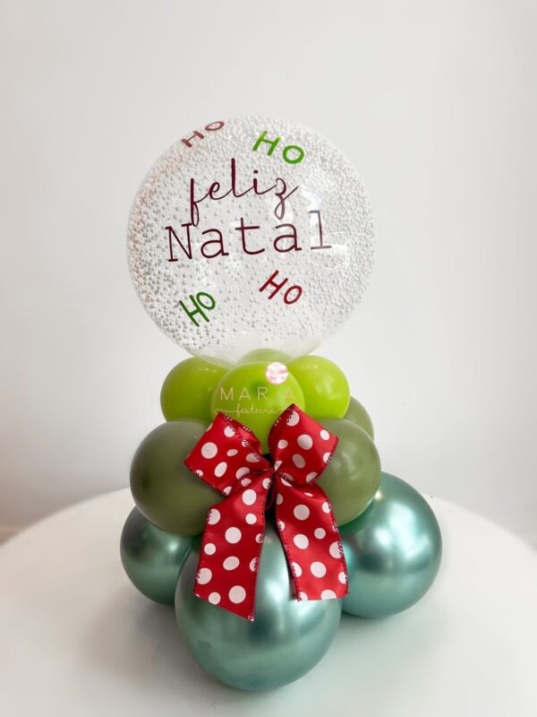 Arranjo de mesa natalino com base em formato de mini árvore de balões, laço decorativo vermelho com poás brancos e mini bubble transparente personalizado com ‘Feliz Natal’ e ‘Ho Ho Ho’.