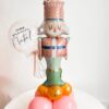 Arranjo decorativo com balão inflável de soldadinho de chumbo, base de balões coloridos e mini bubble personalizado com a frase ‘Meu Primeiro Natal’, ideal para decoração de mesas natalinas.