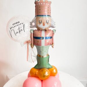 Arranjo decorativo com balão inflável de soldadinho de chumbo, base de balões coloridos e mini bubble personalizado com a frase ‘Meu Primeiro Natal’, ideal para decoração de mesas natalinas.