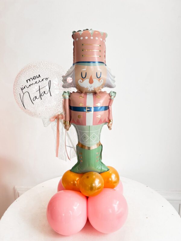 Arranjo decorativo com balão inflável de soldadinho de chumbo, base de balões coloridos e mini bubble personalizado com a frase ‘Meu Primeiro Natal’, ideal para decoração de mesas natalinas.